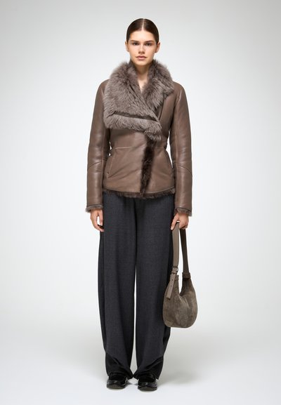 Giacca di pelle marrone con colletto in pelliccia grigia, abbinata a pantaloni oversize grigi scuri e una borsa marrone a textura morbida.