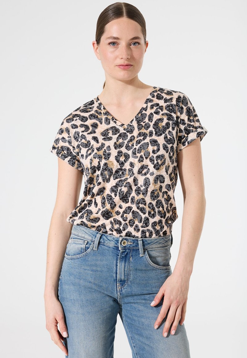 Camiseta de manga corta con cuello en V de estampado de leopardo en beige y negro, hecha de un tejido suave. Combinada con unos jeans de mezclilla azul claro.