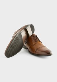 Zapatos de vestir de cuero marrón con un diseño elegante, punta afilada, cierre con cordones, suela de goma texturizada y detalle del tacón en contraste.