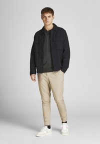 Marinblå knappjacka över en grå tröja, beige avsmalnande byxor och vita sneakers. Har två bröstfickor, släta tyger och en avslappnad passform.