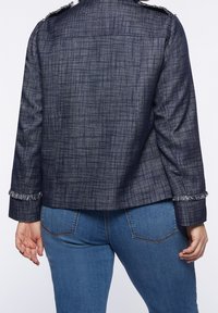 Marinblå texturerad jacka med fransade muddar och axeldetaljer. Har en boxig passform och vävt tyg, kombinerad med ljusblå jeans.