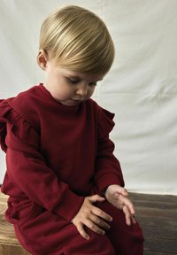 Sudadera de algodón roja con mangas con volantes y pantalones a juego. La tela parece suave con una textura lisa, y el conjunto tiene un corte relajado.