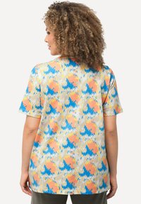 Top de manga corta, de corte holgado, con un patrón de zigzag colorido en tonos de naranja, azul y amarillo sobre un fondo claro. Tejido suave.