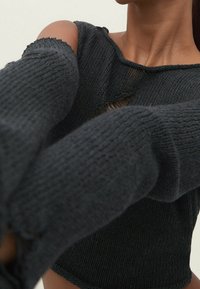 Close-up of a person wearing a dark knitted sweater with large torn holes on the shoulder and sleeve areas.