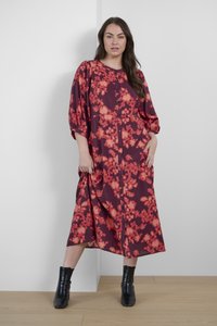 Robe à motif floral rouge avec une coupe décontractée, un col rond et une fermeture à boutons, dotée de manches bouffantes et d'un ourlet au genou. Bottines noires.