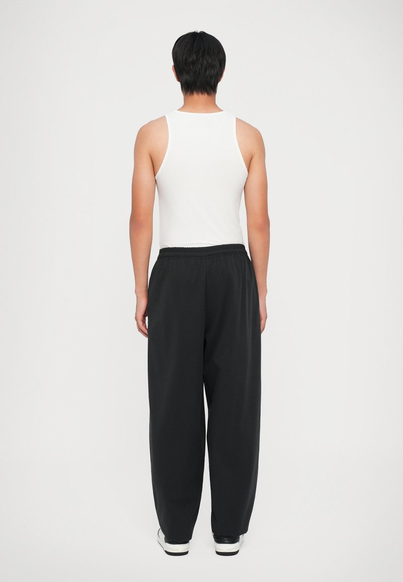 Hvid tanktop parret med løstsiddende sorte bukser. Outfittet har et elastisk taljebånd og er suppleret med hvide og sorte sneakers.