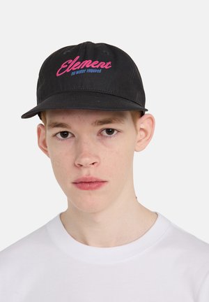 Giovane uomo che indossa un cappellino nero con la scritta rosa "Element" e la scritta blu "no water required" e una t-shirt bianca semplice con collo a giro, sfondo neutro.