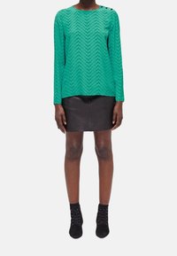 Green textured long-sleeve top with chevron pattern, complemented by a black mini leather skirt and black lace-up ankle boots.