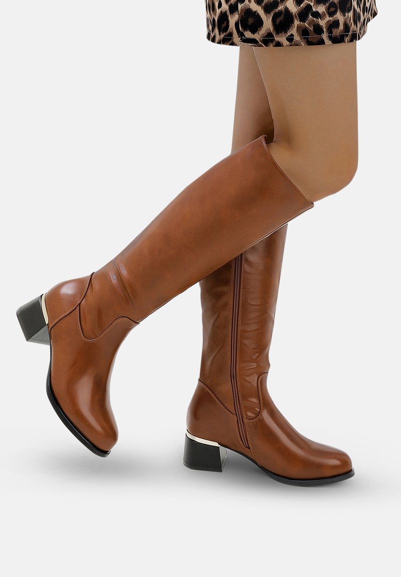 Botas marrones hasta la rodilla, hechas de material sintético liso, con un tacón cuadrado y cremallera lateral. Con detalle metálico en el tacón.