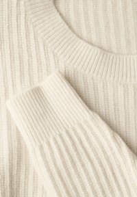 Crème kleurige geribbelde trui met een ronde hals. Kenmerkt zich door dikke, gestructureerde garen en opvallende ribbels op het lichaam en de mouwen.