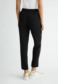 Czarne sportowe spodnie z elastycznym pasem, bocznymi zamkami i zwężanymi nogawkami. Połączone ze złotymi sneakersami i białą bluzką.