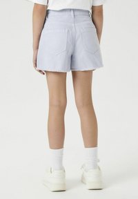 Shorts en denim bleu clair avec un ourlet effiloché, deux poches arrière et une taille ajustée, associés à des chaussettes blanches et des baskets.