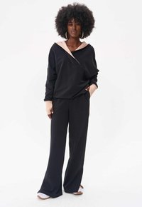 Czarny sweatshirt z jasnoróżowym kapturem, w połączeniu z czarnymi spodniami z szeroką nogawką. Miękka tkanina wydaje się lekko teksturowana, cechuje się luźnym krojem i kieszeniami.