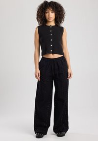 Musta ribbed crop top napit edessä; yhdistetty mustiin leveisiin housuihin, joissa on leikattuja kuvioita ja nauhavyö.