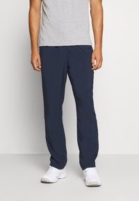 Calças de treino azul marinho em tecido leve, com um corte descontraído, cintura elástica e pernas ajustadas. Combinadas com uma t-shirt cinza e ténis brancos.