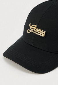 Casquette noire au design structuré, arborant un logo "Guess" doré scintillant à l'avant. Texture du tissu lisse, avec une visière incurvée.