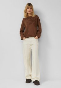Pull marron à manches longues avec motif floral, associé à un pantalon crème à jambes larges et des chaussures à enfiler marron foncé. Coupe simple et décontractée.