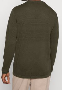 Olivgrüner Strickpullover mit strukturierten horizontalen Streifen und Rundhalsausschnitt, ausgestattet mit gerippten Bündchen und einem leicht verlängerten hinteren Saum.