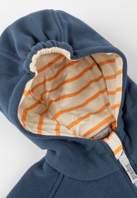 Fleecejacke mit einem navyfarbenen Außenmaterial und einer orangegestreiften Baumwollfütterung. Sie verfügt über eine geraffte, verstellbare Kapuze und einen Frontreißverschluss.