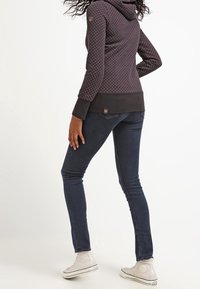 Sudadera de color púrpura oscuro con lunares blancos, textura de la tela visible; combinada con jeans ajustados azules y zapatillas blancas. La sudadera cuenta con cordones.