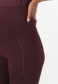 Leggings bordô de cintura alta com um bolso lateral, textura suave e costuras em contraste ao longo das emendas. Design flexível e ajustado ao corpo.