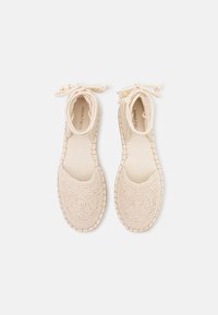 Scarpe in beige allacciate in crochet con punta rotonda, tomaia testurizzata e suola cucita. Fodera in tessuto morbido e delicati dettagli a fiocco.