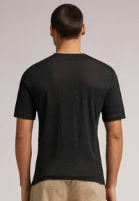 Černé tričko s krátkým rukávem, čistý design, kulatý výstřih, jemná textura a decentní švy, nošeno s khaki šortkami.