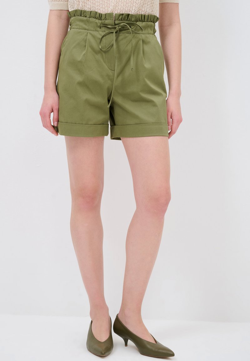 Bermuda verde oliva con fascia arricciata in vita e cordoncino, con pieghe frontali e orli arrotolati. Materiale in cotone liscio.
