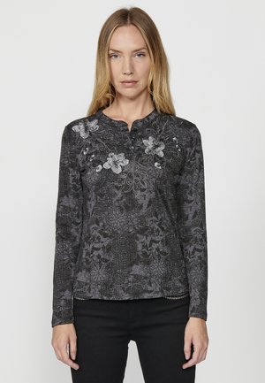 Haut noir à manches longues avec broderies florales, tissu texturé et col boutonné. Présente un motif détaillé et un ourlet légèrement arrondi.