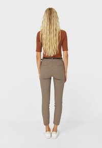 Chemise ajustée marron, pantalon à carreaux marron et crème, coupe slim, avec poches arrière, porté avec des baskets blanches, vu de dos.