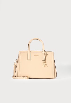 Sac à main en cuir beige Michael Kors avec poignées supérieures, bandoulière amovible et breloque logo MK dorée sur le devant.