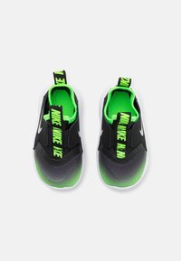 Baskets slip-ons noires et grises avec une tige texturée, des accents verts et un branding noir bien visible sur le talon et la languette. Semelle extérieure blanche.