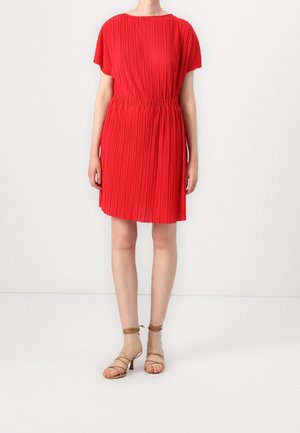 Red pleated dress with short sleeves and elastic waist. Smooth texture, knee-length, paired with tan strappy heels. Minimalist design.