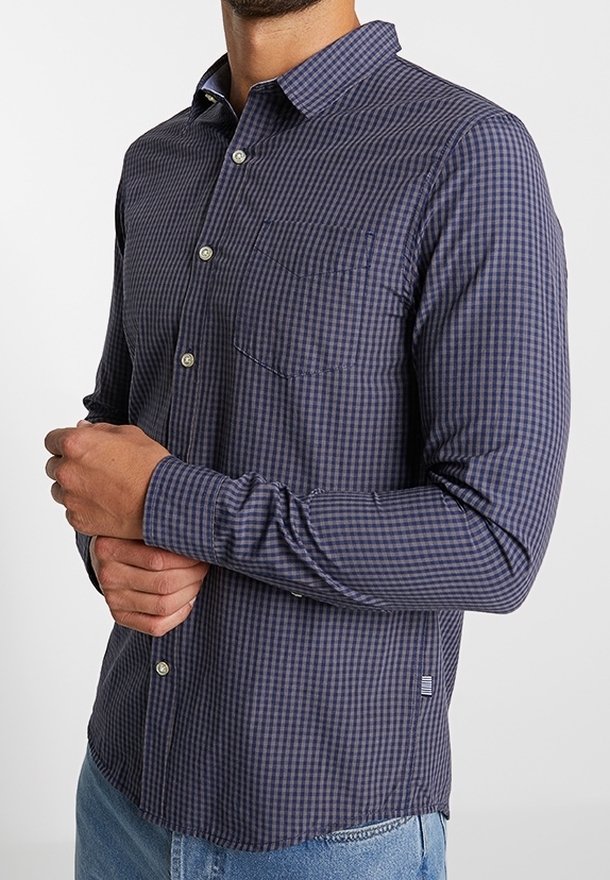 Homme portant une chemise à carreaux bleu marine et noir à manches longues avec boutons, une poche avant et un jean bleu clair.