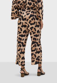 Pantalons à pattes larges en imprimé léopard beige et noir, avec une taille élastique et une longueur raccourcie. Associés à des sandales à talons noires.