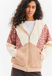 Kurtka z kapturem zapinana na zamek w kolorach kremowym, różowym i brązowym, z geometrycznym wzorem, z nakrapianym wzorem na rękawach i miękką fakturą.