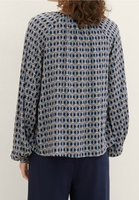 Blouse bleu marine avec motif géométrique en blanc et rose clair. Manches longues avec poignets froncés, coupe décontractée et tissu doux et fluide.