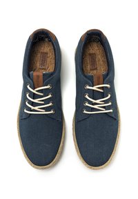 Zapatillas de lona azul marino con cordones crema, que cuentan con un acento de cuero marrón en la lengüeta y una plantilla de corcho texturizado. Suela de yute estilo espadrille.