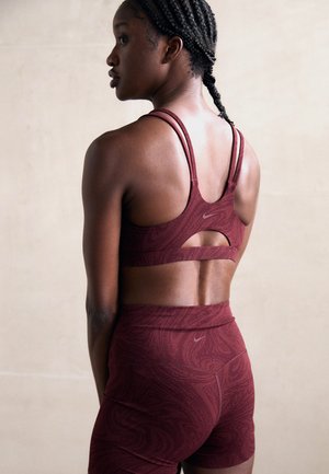 Maroon sports bra and shorts set featuring a textured pattern, racerback design with cutout detail, and Nike logo.