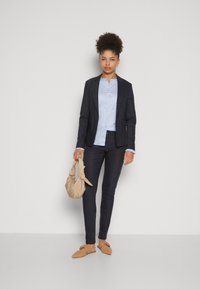 Námořnický blazer a úzké kalhoty, světle modrá košile, béžová taška a slip-on boty s mašlí. Hladká tkanina s přizpůsobeným střihem.
