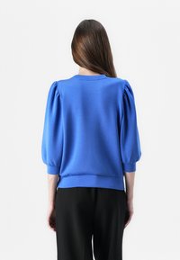Pullover blu con maniche a palloncino, scollatura rotonda e orlo a coste. Realizzato in tessuto liscio, il design presenta un colore uniforme e una vestibilità morbida.
