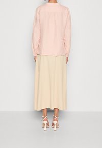 Lichtroze langemouwen shirt, losse pasvorm met een rugplooidetail, gecombineerd met een vloeiende, crèmekleurige maxirok en witte gespsandalen met blokhak.