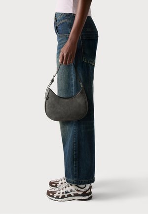 Borsa a tracolla grigia in pelle compatta con forma curva, manico corto e cuciture a contrasto, abbinata a jeans in denim scuro a vita alta e sneakers.