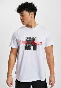 Hvit bomulls-T-skjorte med et sentralt svart-hvitt grafisk motiv og rød tekst "Pain to Power." Kortermet og rund hals.