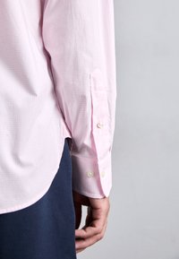 Světlé růžové kostkované polodlouhé tričko s manžetami na knoflíky, zakulaceným lemem a hladkou texturou látky. Nosit přes námořnické kalhoty.