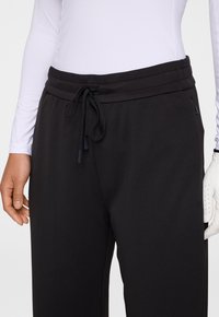 Svarta sportbyxor i texturerad tyg, med snörning i midjan och sidofickor, i kombination med en åtsittande långärmad tröja.