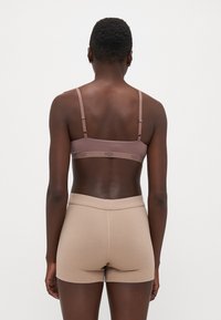 Smeđa UGG bralette s podešivim trakama, elastičnom trakom s logotipom i rebrastim bež hlačicama. Glatka tkanina; bez vidljivih uzoraka ili ukrasa.