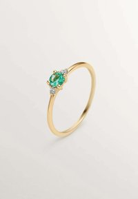 Anillo de oro con una gema verde ovalada, acentuada por dos piedras claras más pequeñas a cada lado, con una banda lisa y pulida.