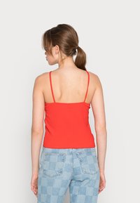Camisola de alças finas, com riscas vermelhas, combinada com calças de ganga de cintura alta em xadrez azul claro. Textura suave, design ajustado.