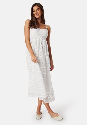 Abito maxi bianco in pizzo con spalline regolabili, un busto aderente e una gonna fluida. Presenta un motivo floreale su tutta la superficie.
